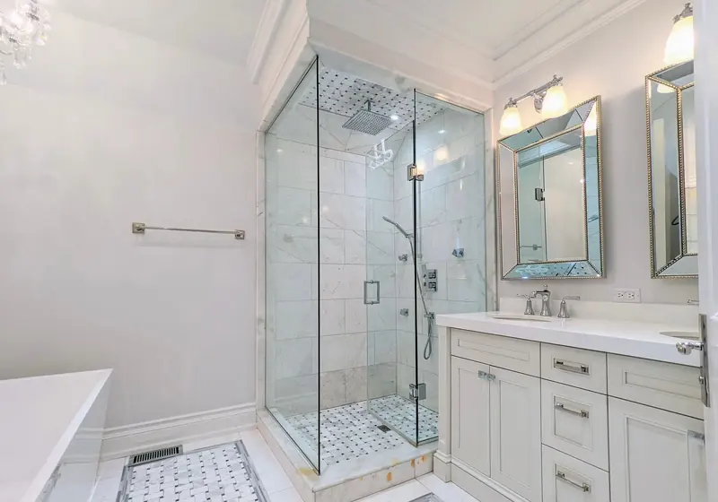 An ensuite with a frameless glass shower, marble-look tile and a white vanity.