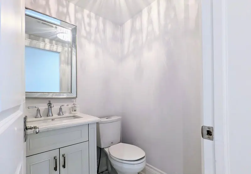 A powder room with a framed mirror, a white vanity and a toilet.