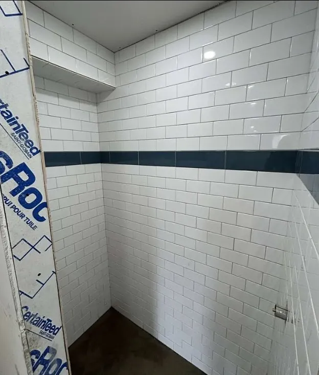 The same shower finished in white subway tile with a dark accent band.