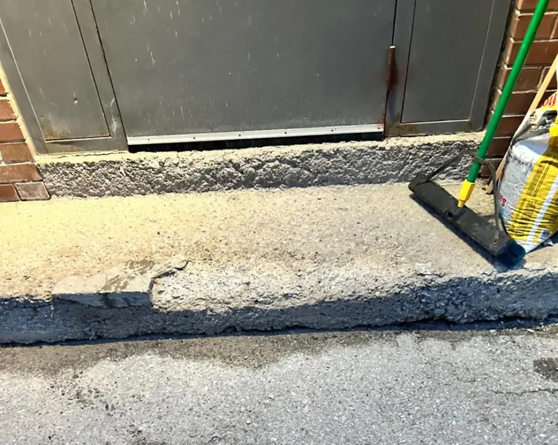 A crumbling concrete step at a grey service door.