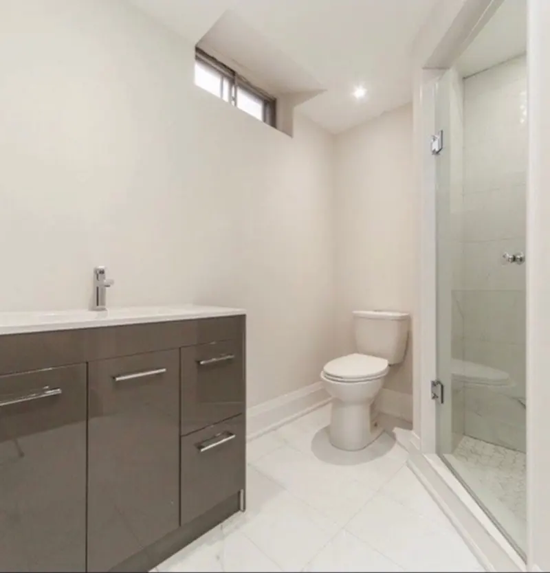 A bathroom with a glossy grey vanity, white marble-look tile and a glass shower.