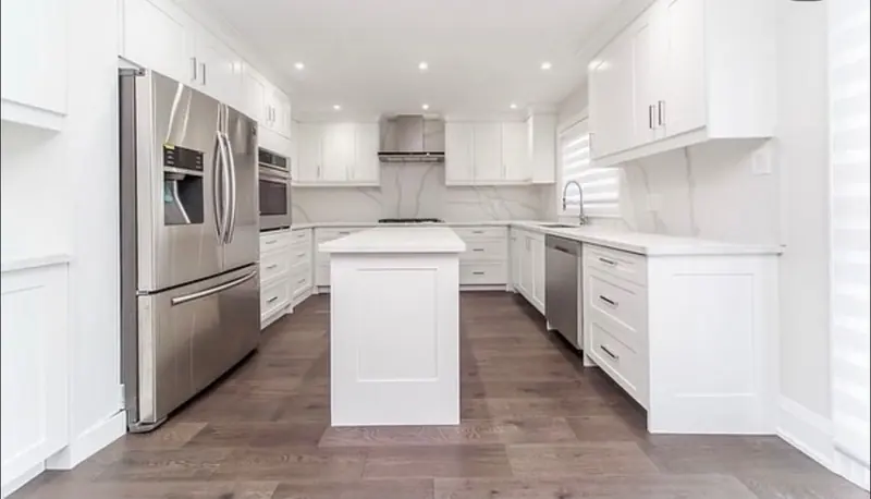 A white shaker kitchen with custom cabinets to the ceiling, an island and a marble backsplash.