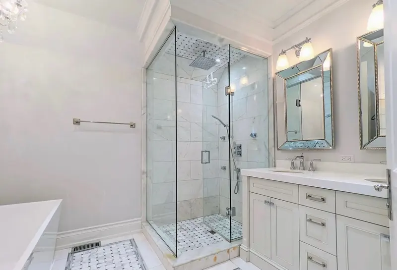 An ensuite with a glass shower in marble tile, a white double vanity with bevelled mirrors and a freestanding tub.